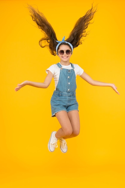 Amazing long hair Cute small girl with long hair jumping on yellow background Adorable little child enjoy long brunette hair Best hairstyle for long hair Beauty salon Hairdressers parlor