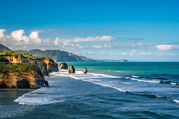 Amazing Rock formations the three sisters on Tongaporutu beach lined by huge cliffs  and the volcanic mountain