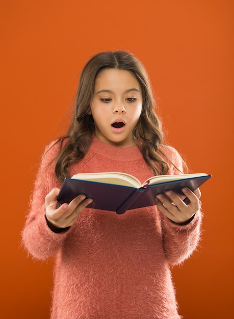 Amazing story. Girl hold book orange background. Child show book notepad. Book store. Free book available to read. Interesting literature. Development and education. Child care and happy childhood.