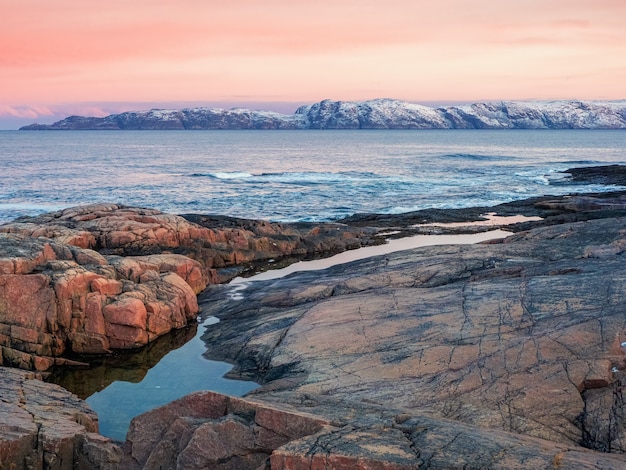 Amazing sunrise landscape with polar white snowy range of mountains. Wonderful mountain landscape with a gorge and a Cape on the shore of the Barents sea. Teriberka