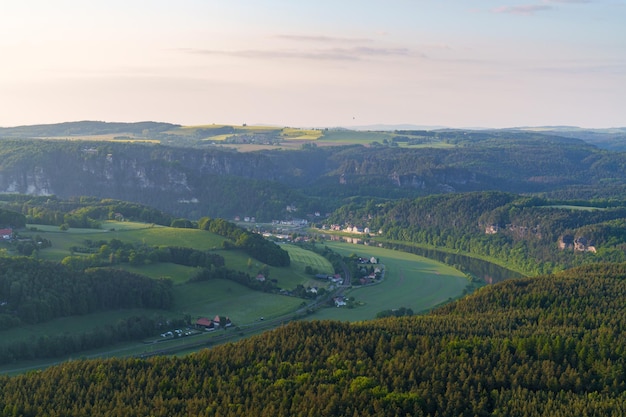 Amazing view from the cliff A picturesque landscape with cozy houses green yellow meadows the Elbe River Beautiful mountain landscape Saxon Switzerland Lilienstein sunrise long shadows