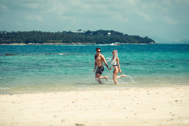 Amazing young couple runs on the beach hand in hand