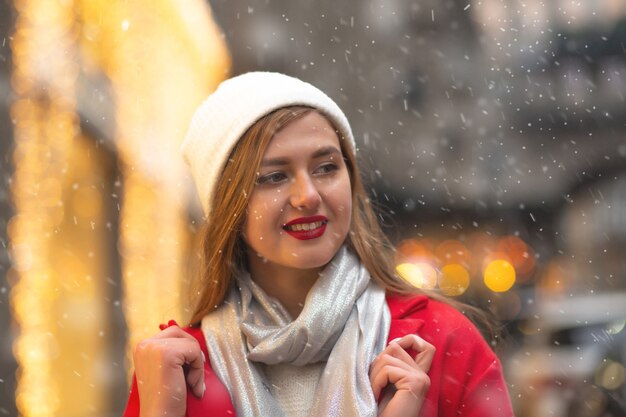 Amazing young woman in red coat walking at the street fair during the snowfall