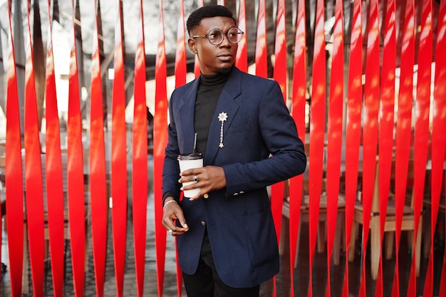 Amazingly looking african american man wear at blue blazer with brooch black turtleneck and glasses posed at street Fashionable black guy with cup of coffee