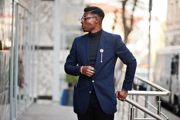 Amazingly looking african american man wear at blue blazer with brooch black turtleneck and glasses posed at street Fashionable black guy