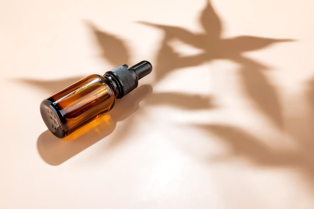 Amber bottle with cannabis oil used for medical purposes on beige background with daylight and the shadow of a hemp leaf Soothing cbd oil Alternative Medicine mockup with copy space