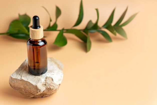 Amber glass bottle of essential oil or serum with pipette on stone podium with and green branch on a beige background Natural skincare cosmetic concept