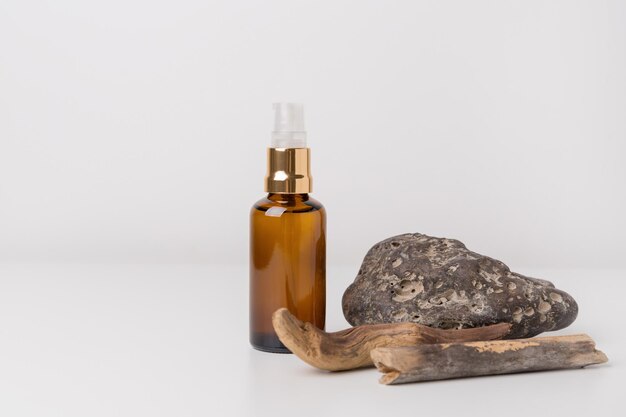 Amber glass bottle with essential oil or face serum and dry branches with rough stone