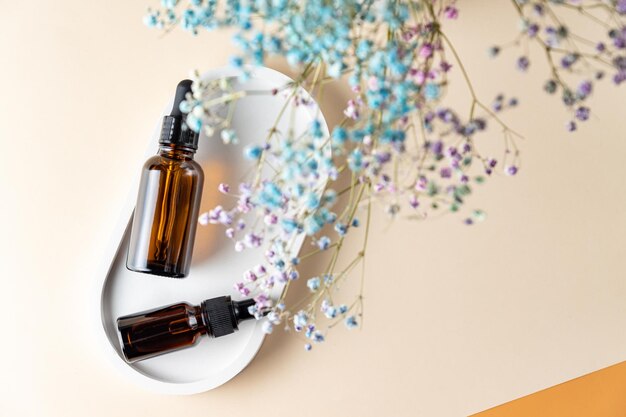 Amber glass bottles with aromatic oil or serum on a stone tray with gypsofila flowers above. Natural Organic Spa Cosmetic concept. Top view.