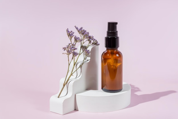 Amber glass dropper bottle on white podium and geometric shapes and dry purple flower on light pink background Skincare products natural cosmetic Containers with crea texture inside