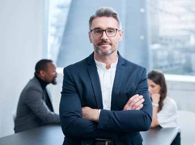 Ambition gets you far I can testify to that Portrait of a confident mature businessman standing in an office with his colleagues in the background