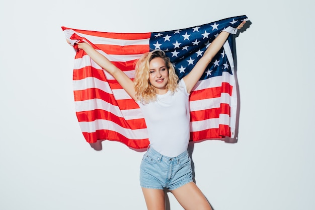 American blonde woman holding the USA flag isolated over a white wall