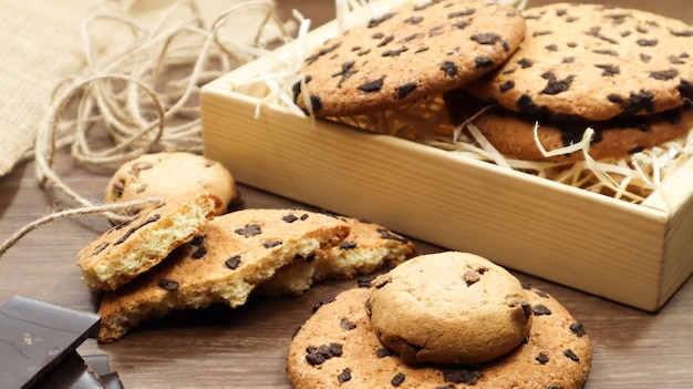 American chocolate chip cookies on a brown wooden table close-up in a box. Traditional rounded crunchy dough with chocolate chips. Bakery. Delicious dessert, pastries. Rural still life.