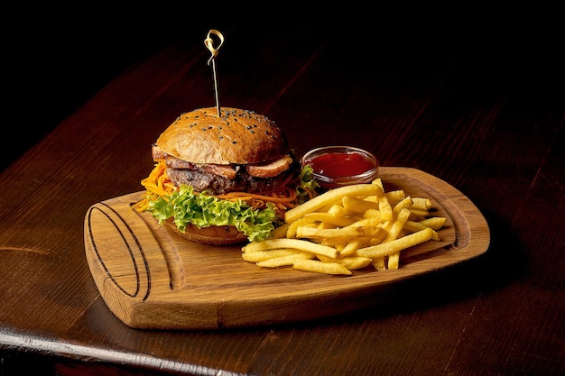 American fast food burger with fries and sauce. Dark wooden background. Selective focus.