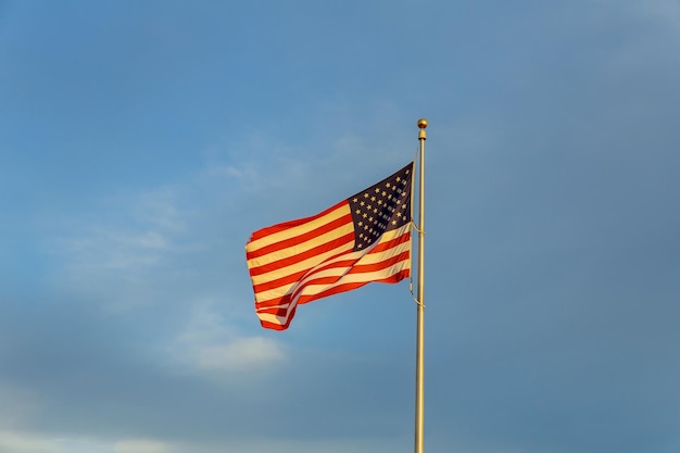 American flag on flagpole waving in the wind against clouds blue sky and the moon