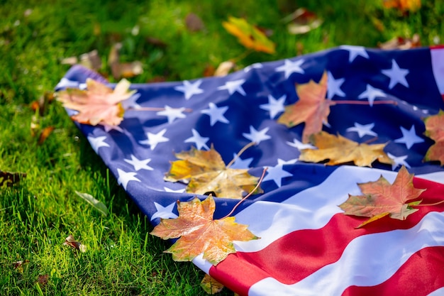 American flag with maple leaves on green grass in autumn