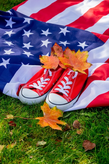 American flag with maple leaves and red gumshoes on green grass in autumn