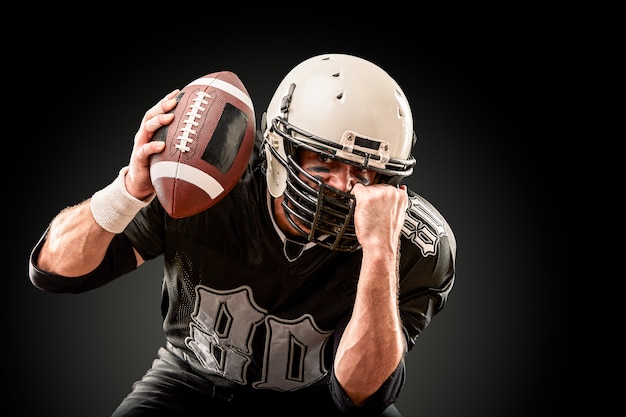 American football player in dark uniform with the ball is preparing to attack