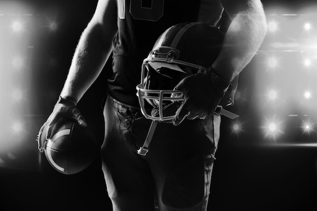 American football player standing with helmet and rugby ball