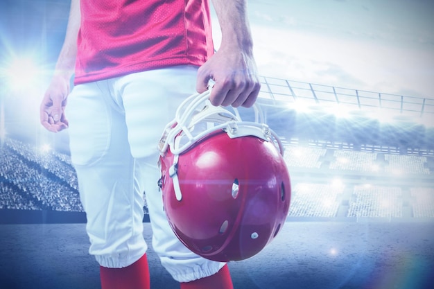 An american football player taking his helmet on her hand  against sports arena