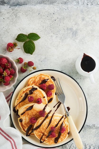 American pancakes Pancakes with fresh raspberry with chocolate glaze or toppings in gray bowl on light gray table background Homemade classic american pancakes Page for magazine concept Top view