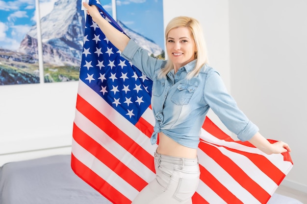 American patriot. Portrait of a happy young woman smiling to you while holding an American flag.