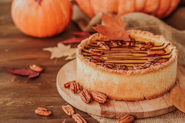 American pumpkin pie decorated with chocolate and pecan nuts on a wooden table