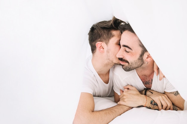 Amorous gay couple cuddling in bed