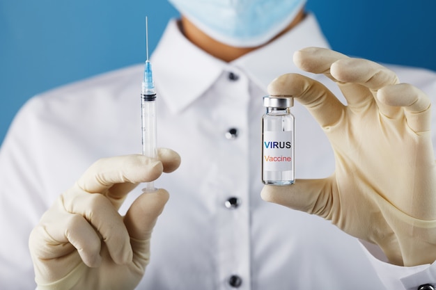 An ampoule with the inscription Virus Vaccine and a syringe in the hands of a scientist doctor