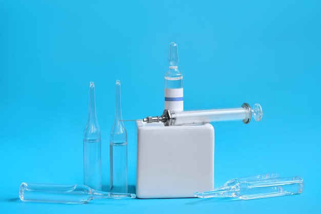 Ampoules with a syringe and a vaccine on a cube stand Bright blue background