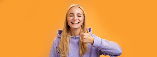 Amused joyful optimistic young excited blond european female model in hoodie smiling broadly close