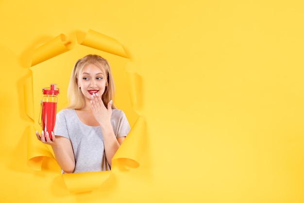 Amused young female looking at red bottle on yellow wall