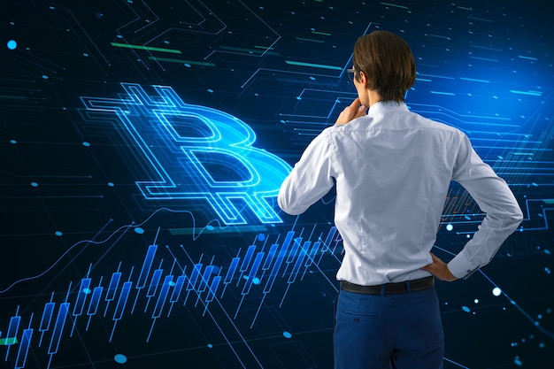 Analytics trading investing and cryptocurrency concept with pensive man back view looking at dark virtual screen with big glowing digital bitcoin sign and financial chart candlestick