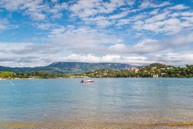 Anchored boat on sea surface against Corfu under blue sky