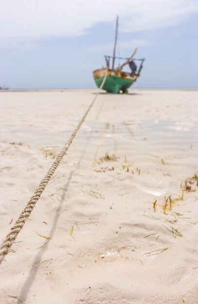 Anchored fishing boat on low tide Indian ocean coast Boat with rope on white sand beach