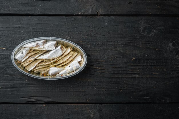 Anchovies canned fish in a tin can seafood set, in plastic container, on black wooden table