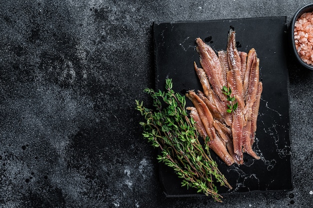 Anchovies fish fillet in Olive Oil. Black table. Top view. Copy space.