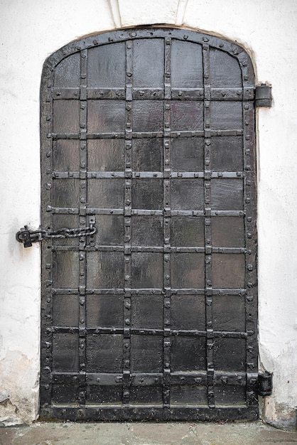 Ancient church door on a white wall Old black metal door of the church with rivets