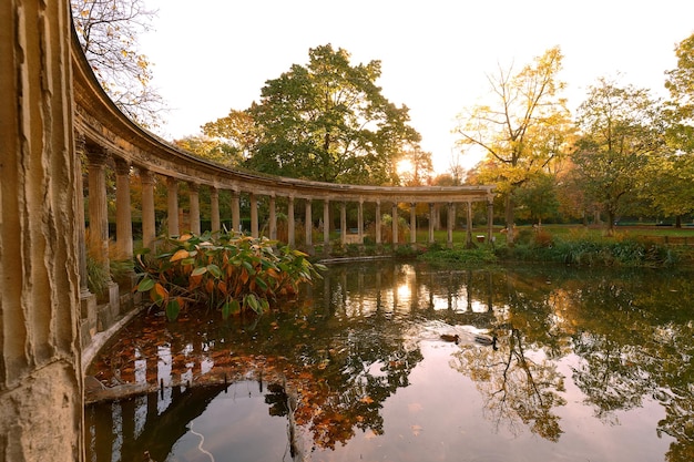 The ancient columns of Parc Monceau are reflected in the water of the oval basin in the sun This public garden is located in the 8th arrondissement of Paris