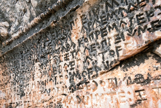 Ancient gray and beige stone wall with carved inscriptions