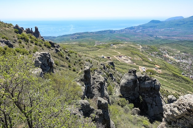 Ancient limestone high mountains of rounded shape in the air haze. The Valley of Ghosts. Demerji. Green trees and bushes in the foreground. May 2021. Crimea.