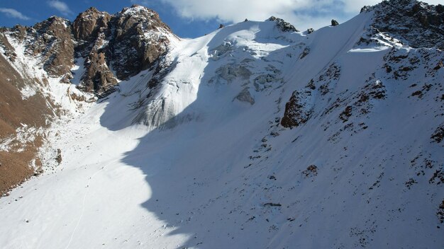 An ancient snow glacier among high mountains. In places there are steep cliffs and large rocks.