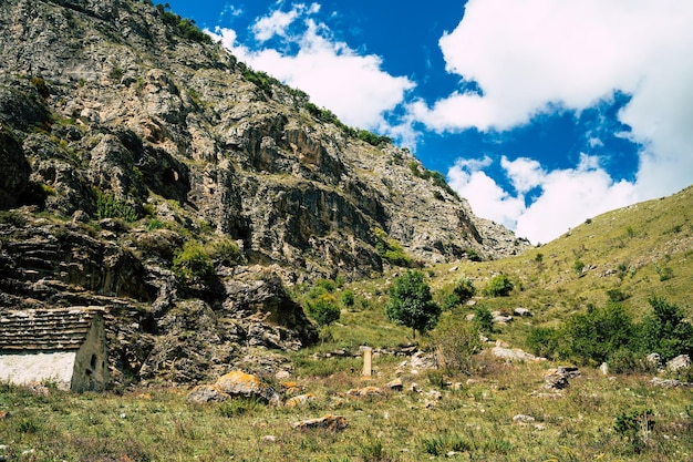 Ancient stone houses in green mountains Amazing landscape with aged stone buildings located on green grassy slope of rocky mountain in sunny summer day