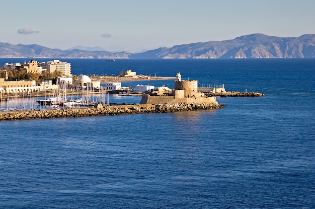 Ancient windmills and castle with lighthouse at the edge of Rhodes harbor in Greece