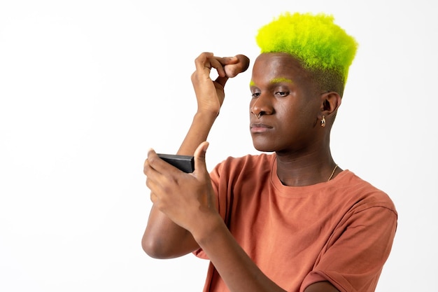 An androgynous black man posing putting on makeup LGTBI concept applying blush with a mirror