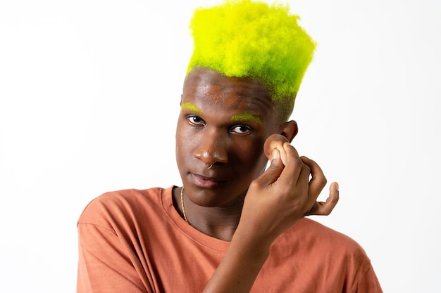 An androgynous black man posing putting on makeup LGTBI concept applying blusher white background