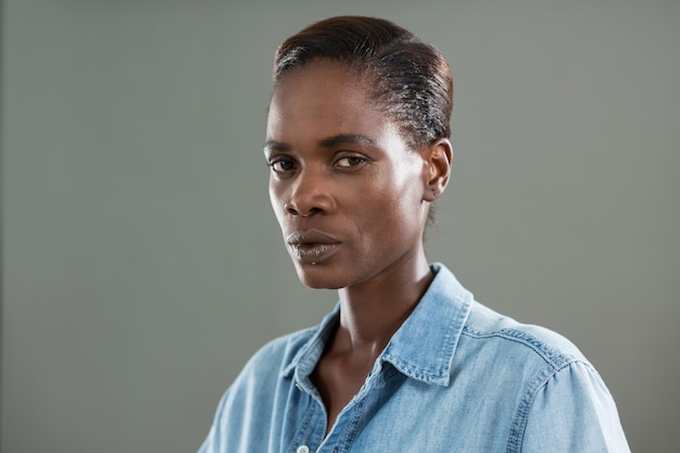 Androgynous man in denim shirt posing against grey wall