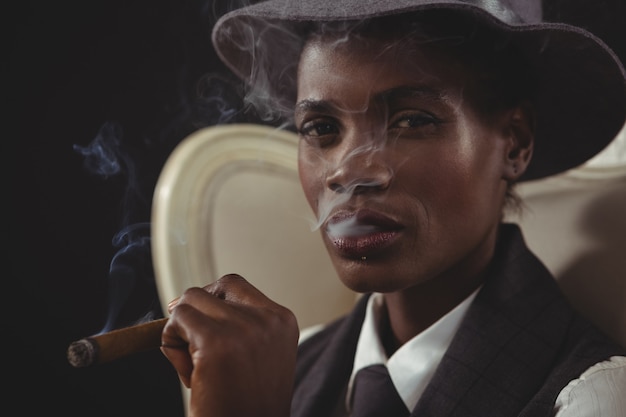 Androgynous man smoking cigar while sitting on a chair