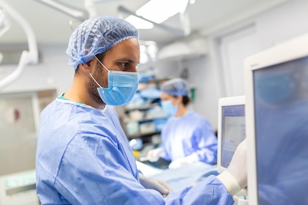 Anesthetist Working In Operating Theatre Wearing Protecive Gear checking monitors while sedating patient before surgical procedure in hospital