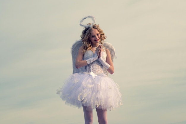 Angel child girl with curly blonde hair innocent girl concept charming curly little girl in white dr...